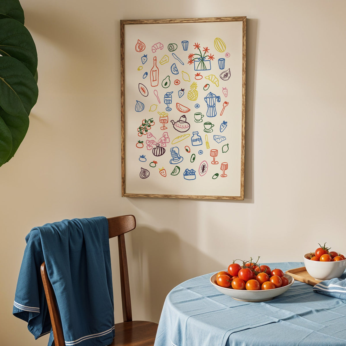 Colorful food doodle print in an oak frame above a blue linen table with ripe tomatoes
