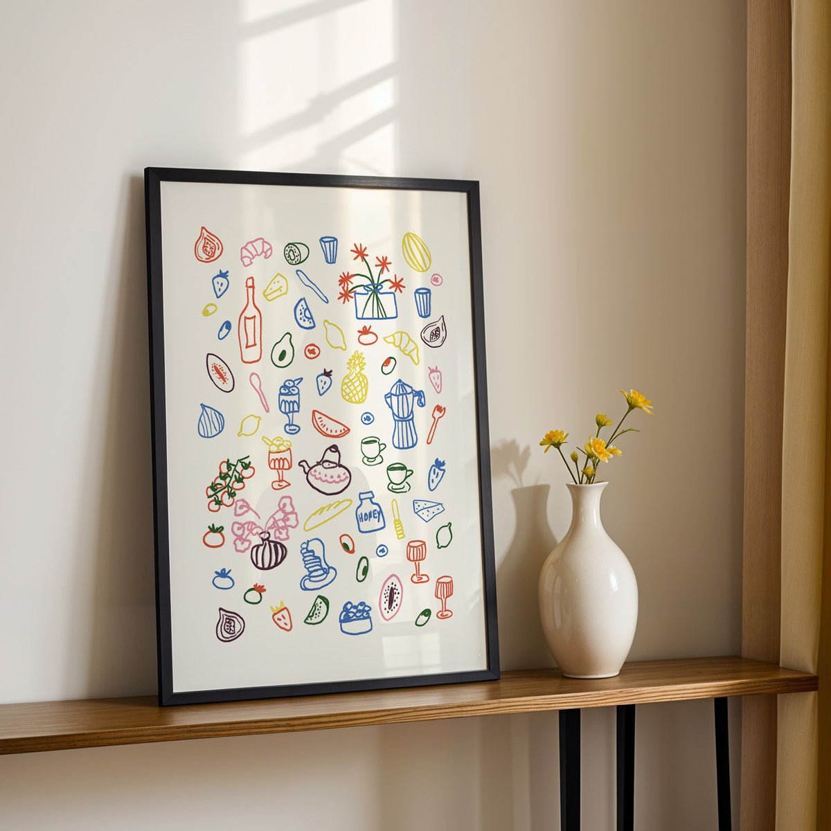 Colorful food doodle print in a black frame on a console table with yellow daisies