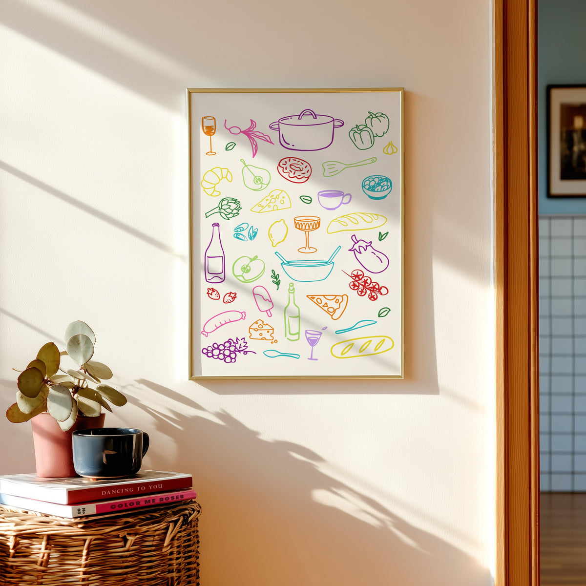 Food doodle print shown in a gold frame above a basket of books and a pilea plant