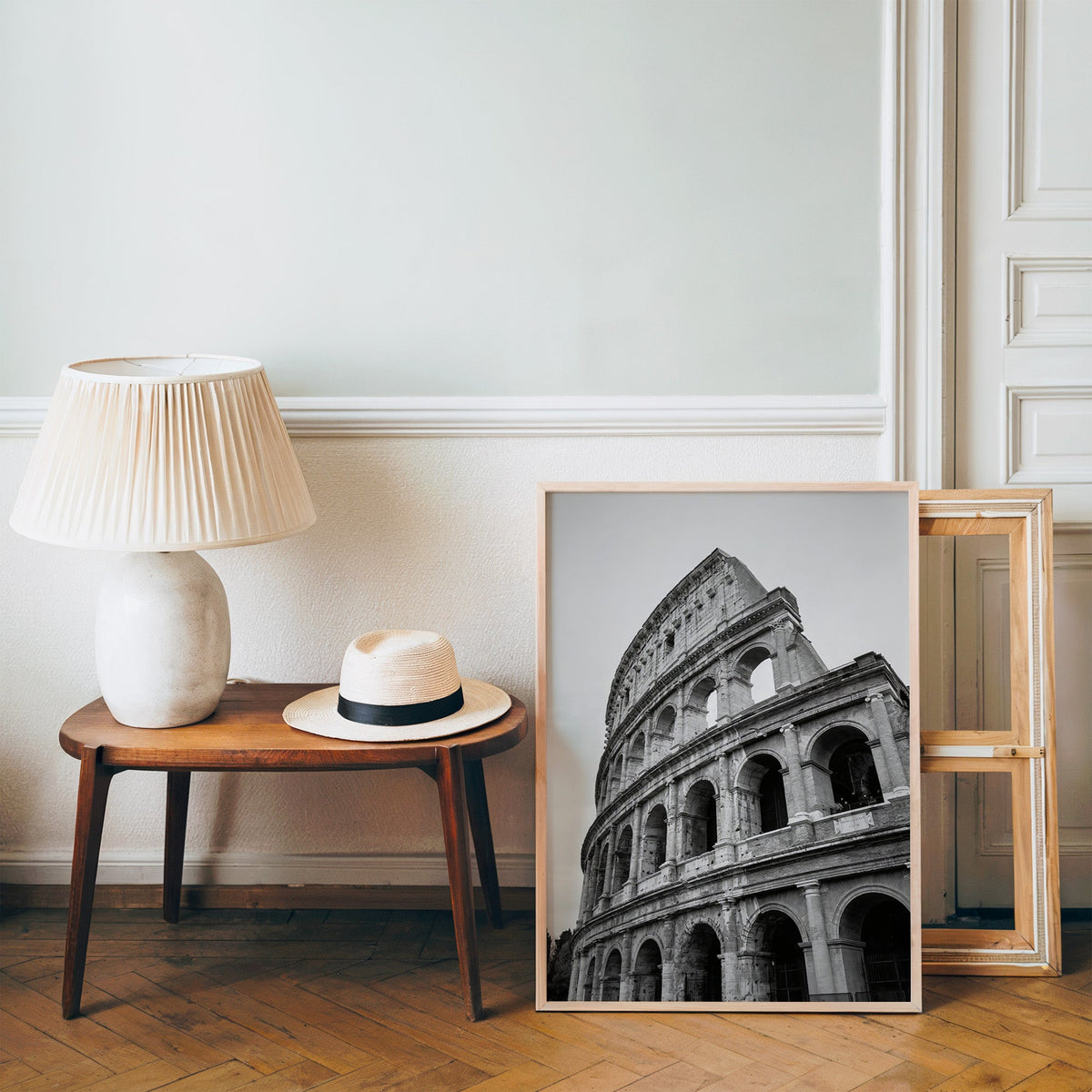 Colosseum Rome arches from below print in a pine frame on a wood floor beside a lamp and straw hat