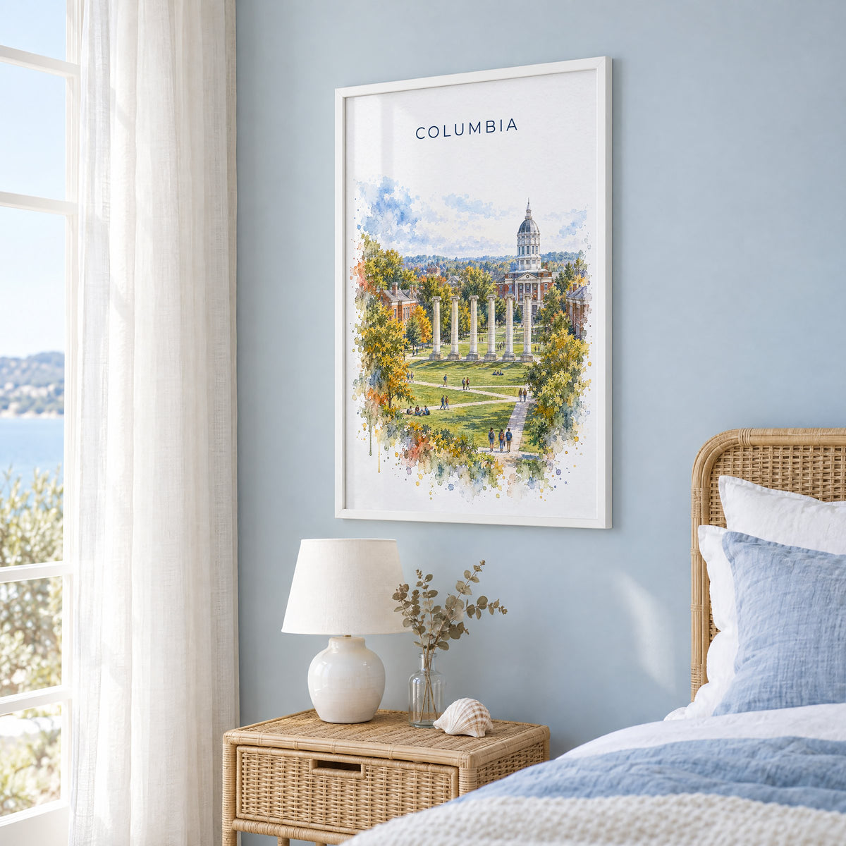 Columbia, Missouri watercolor print in a white frame on a pale blue wall beside a rattan bed in a coastal bedroom