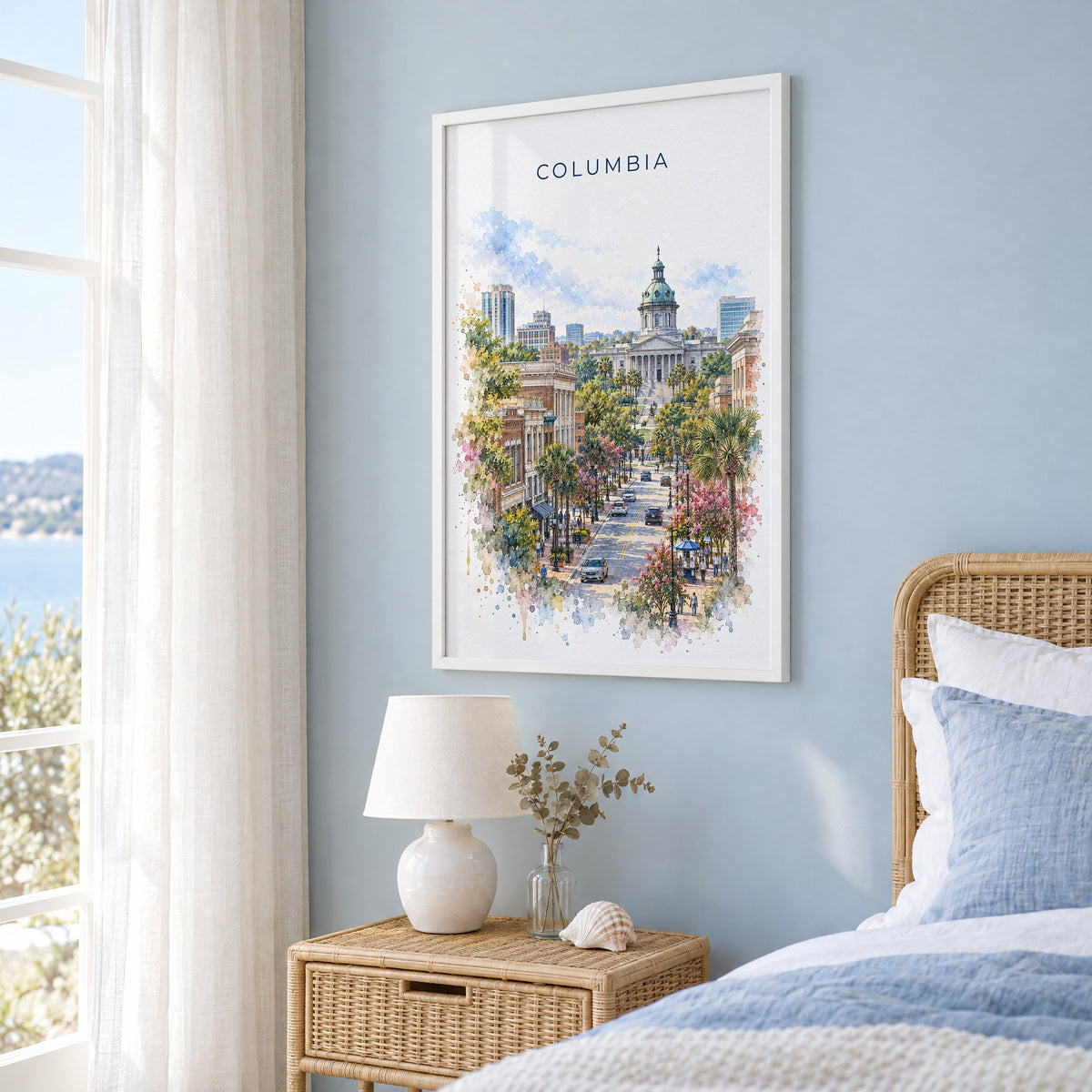 Columbia, South Carolina watercolor print in a white frame on a pale blue wall beside a rattan bed in a coastal bedroom