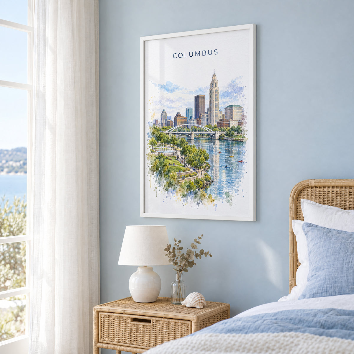 Columbus, Ohio watercolor print in a white frame on a pale blue wall beside a rattan bed in a coastal bedroom