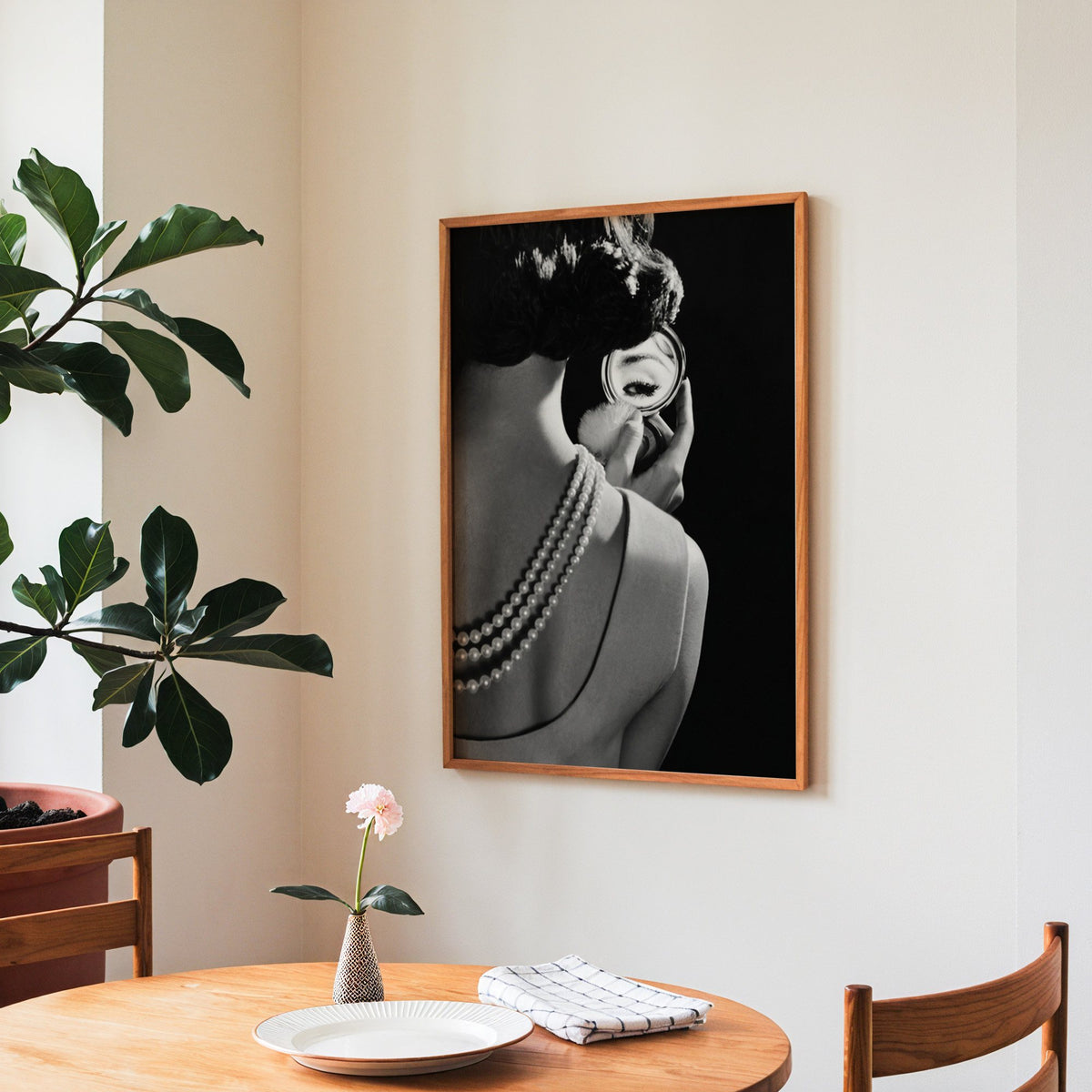 Woman from behind, eye in compact mirror, pearls print in a teak frame above a round wooden dining table