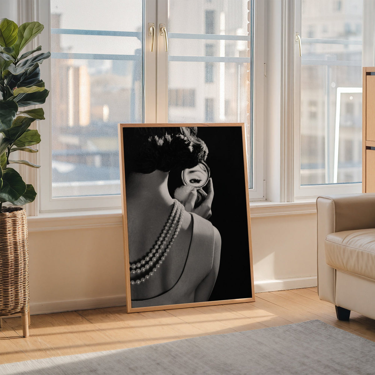Woman from behind, eye in compact mirror, pearls print in an oak frame leaning on the floor beside a fiddle leaf fig