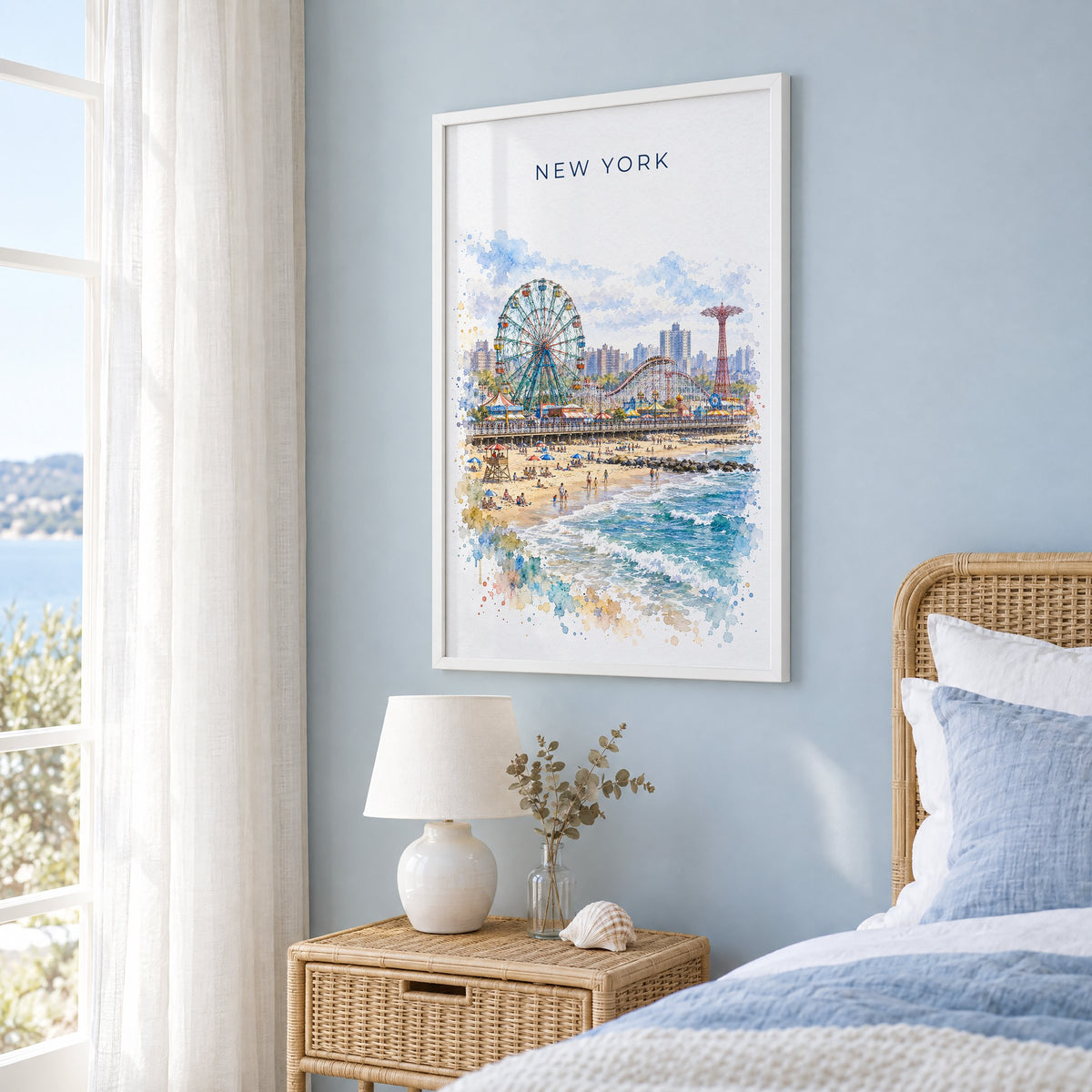 Coney Island watercolor print in a white frame on a pale blue wall beside a rattan bed in a coastal bedroom