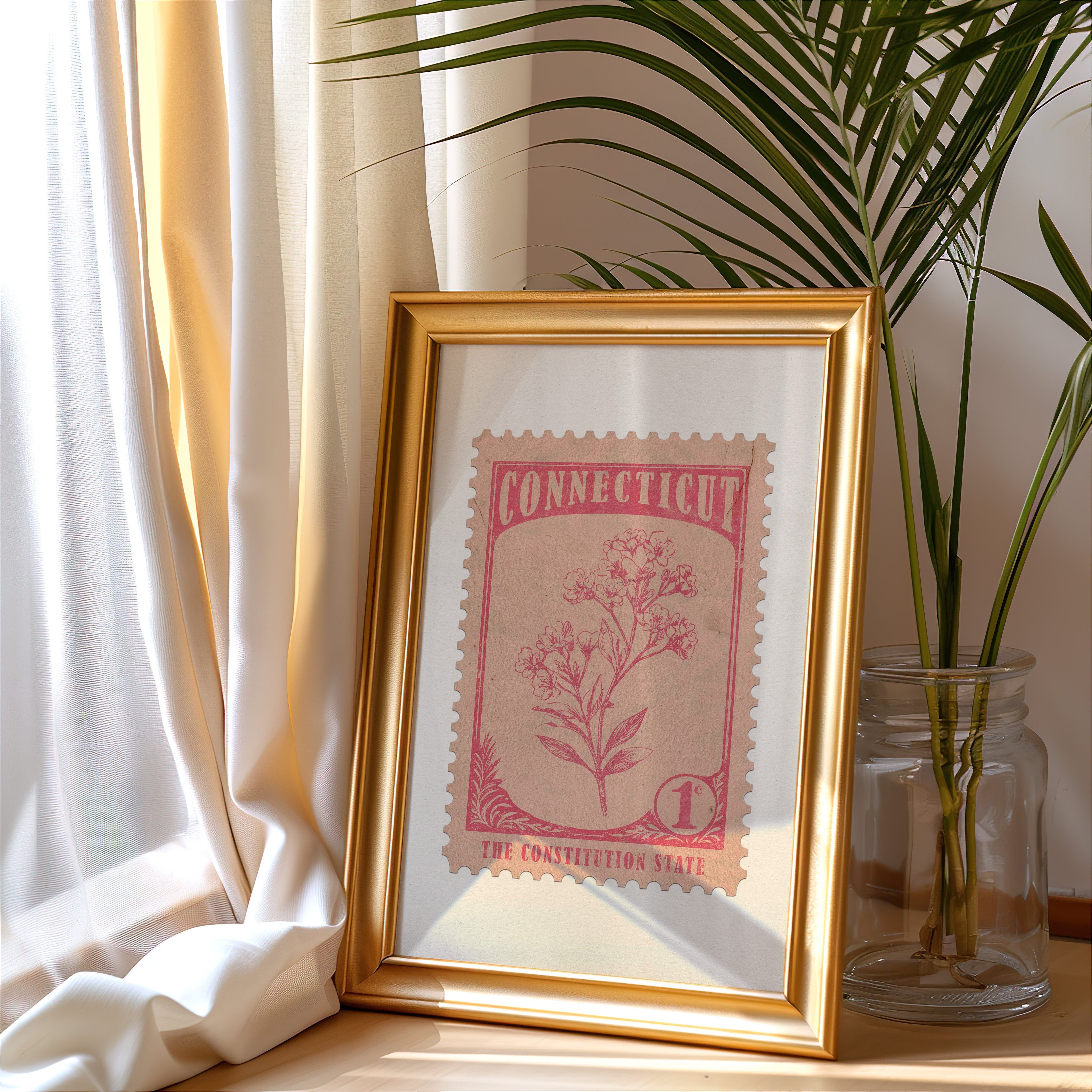 Connecticut stamp print in a gold frame leaning by a cream curtain with a palm in a glass jar