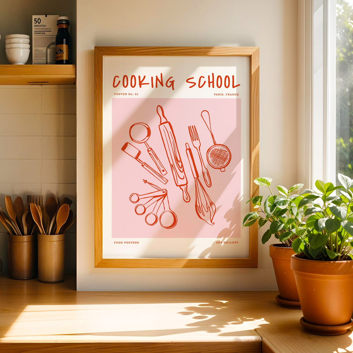 Cooking School utensils print in a light pine frame beside a jar of wooden spoons