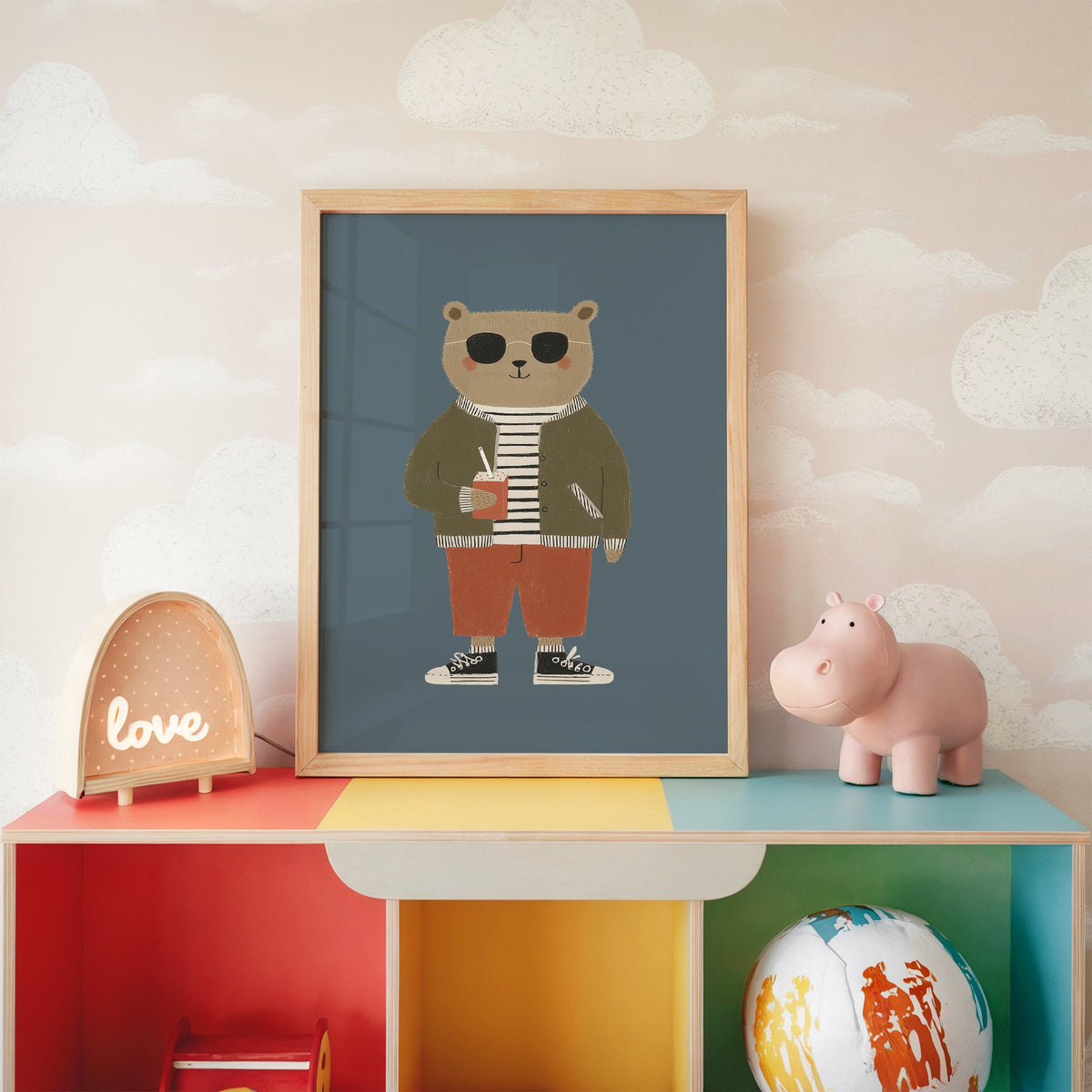 Cool bear sunglasses juice box nursery print in an oak frame on a rainbow toy shelf against cloud wallpaper