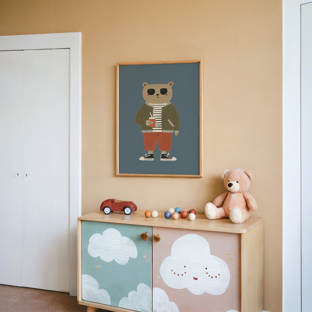 Cool bear sunglasses juice box nursery print in an oak frame on a peach wall above a cloud-painted cabinet