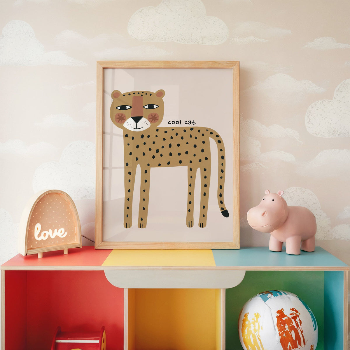 Cool cat cheetah nursery print in an oak frame on a rainbow toy shelf against cloud wallpaper