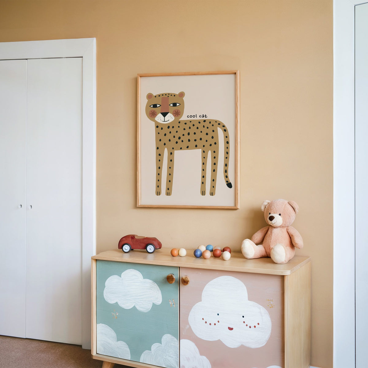 Cool cat cheetah nursery print in an oak frame on a peach wall above a cloud-painted cabinet