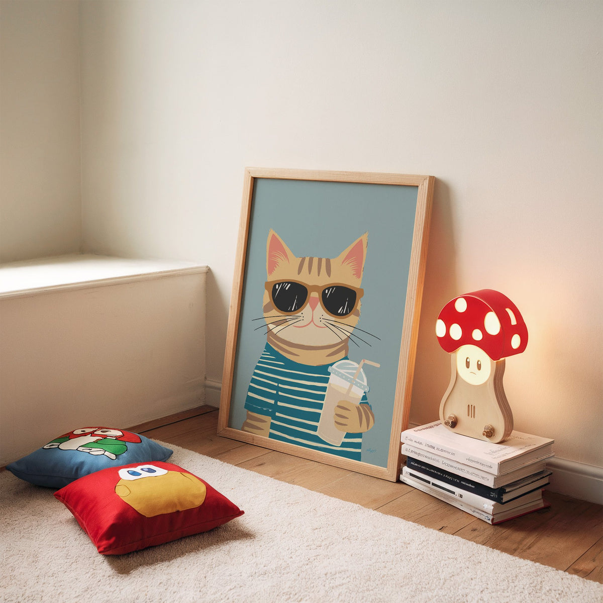 Orange tabby cat with iced drink nursery print in an oak frame leaning on a rug beside a mushroom lamp and floor cushions