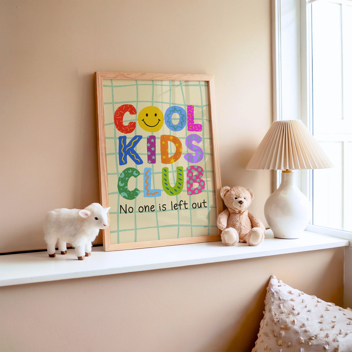 Cool kids club colourful letters nursery print in an oak frame on a window ledge with a toy lamb and teddy