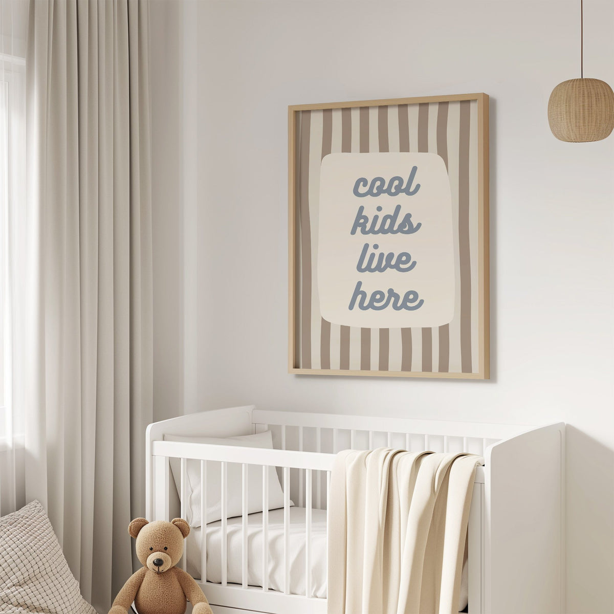 Cool kids live here nursery print in an oak frame above a white crib with a teddy bear