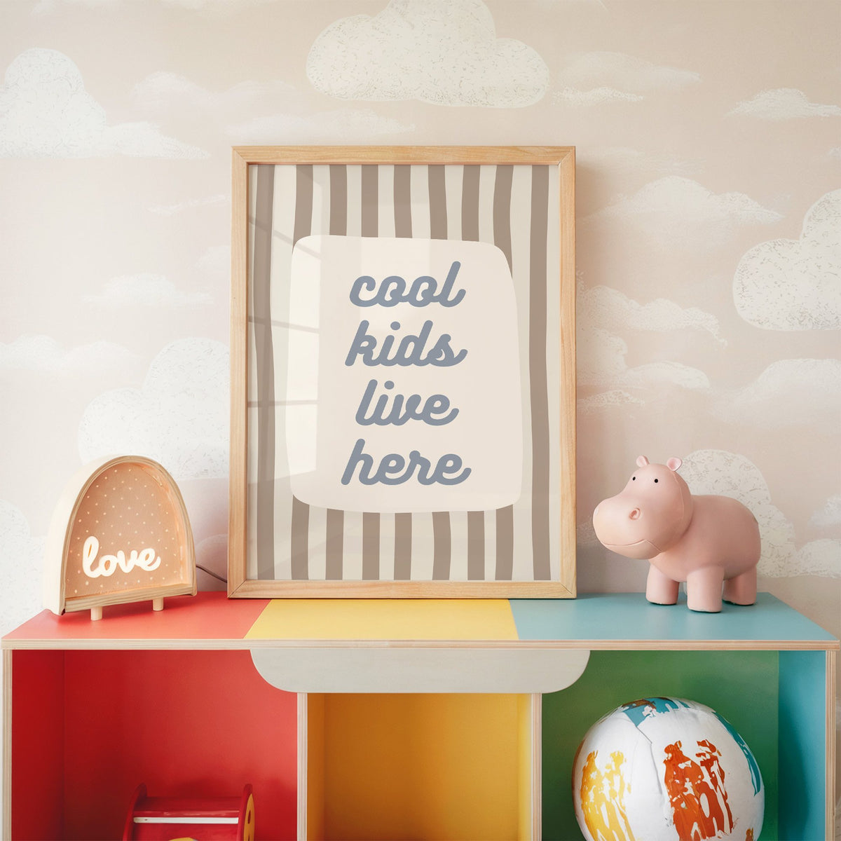 Cool kids live here nursery print in an oak frame on a rainbow toy shelf against cloud wallpaper