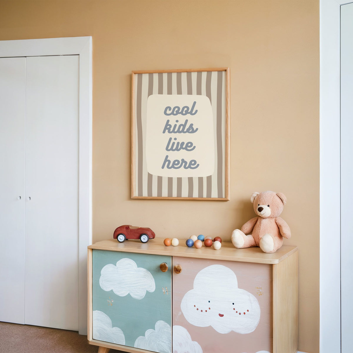 Cool kids live here nursery print in an oak frame on a peach wall above a cloud-painted cabinet