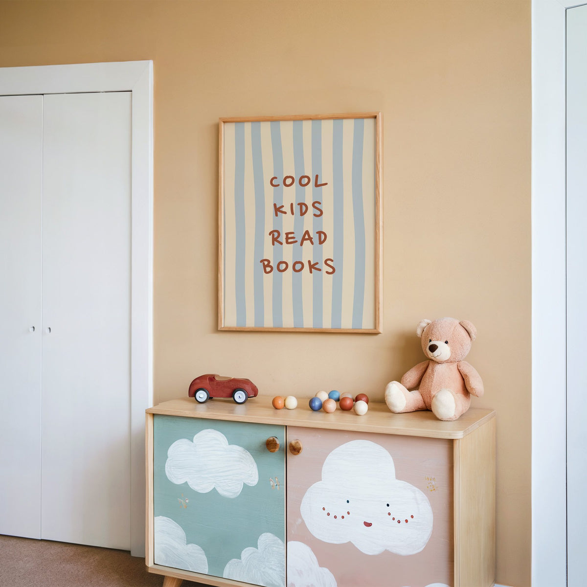 Cool kids read books blue stripe nursery print in an oak frame on a peach wall above a cloud-painted cabinet