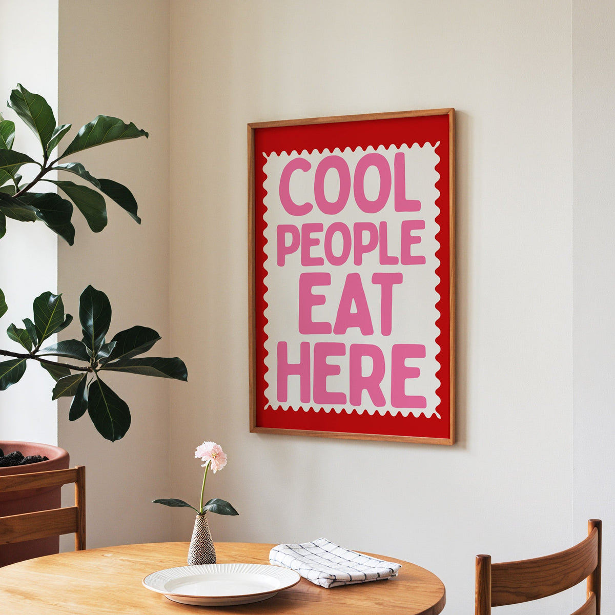 Cool People Eat Here print in a walnut frame above a round table beside a fiddle-leaf fig