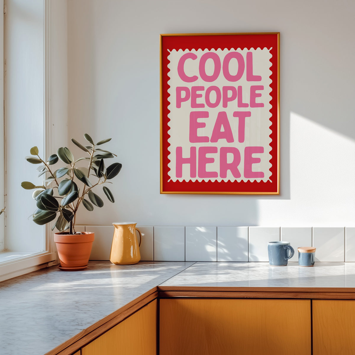 Cool People Eat Here print shown in a gold frame above a marble counter in a tan kitchen