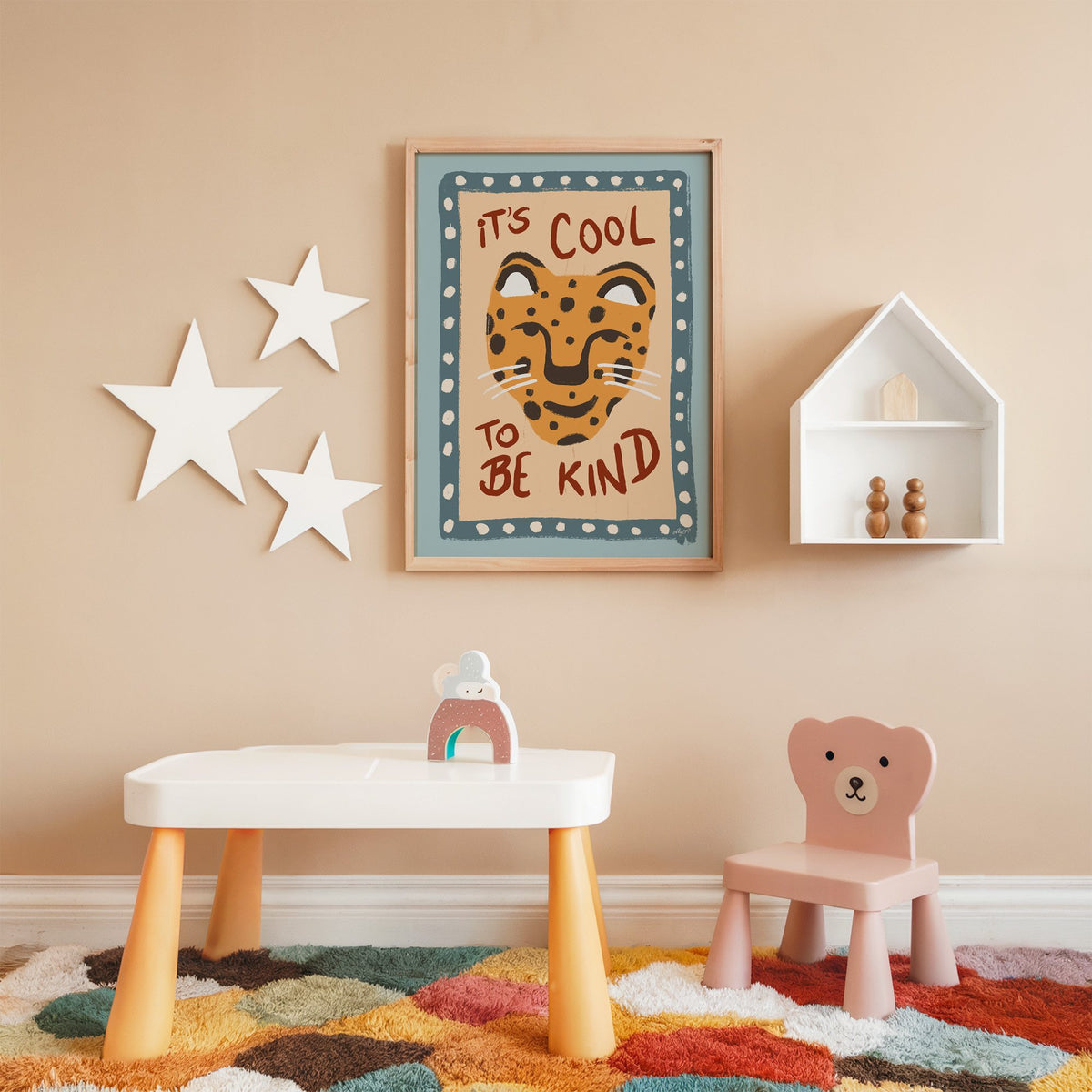 Cool to be kind cat quote nursery print in an oak frame on a peach wall above a kids table with wall stars
