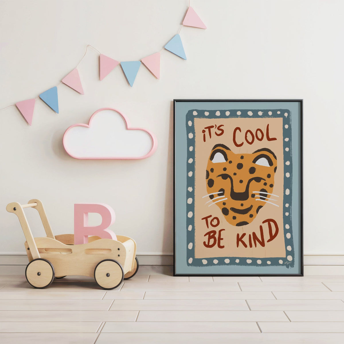 Cool to be kind cat quote nursery print in a black frame under pastel bunting by a wooden baby walker