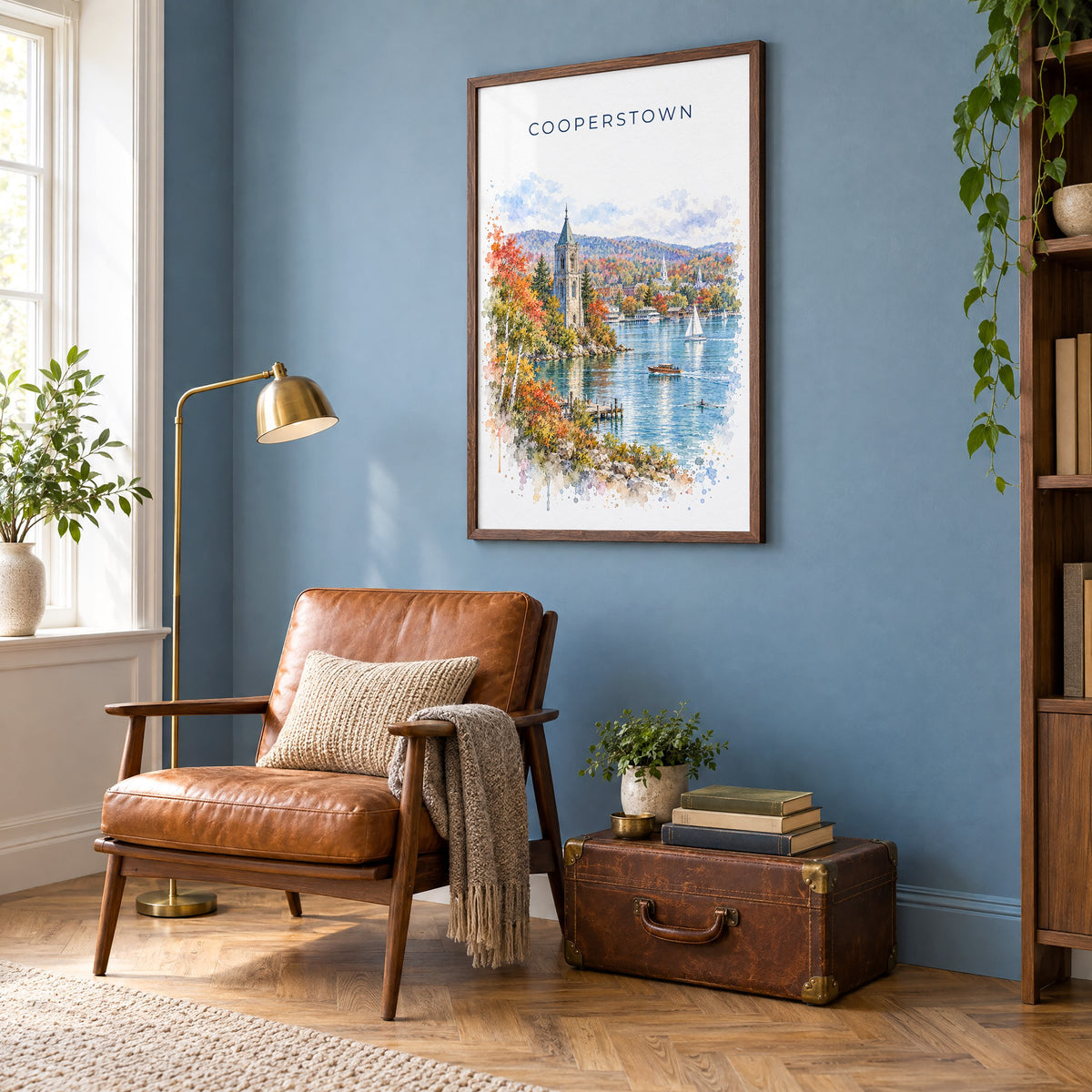 Cooperstown watercolor print in a walnut frame on a blue wall above a leather armchair in a reading nook