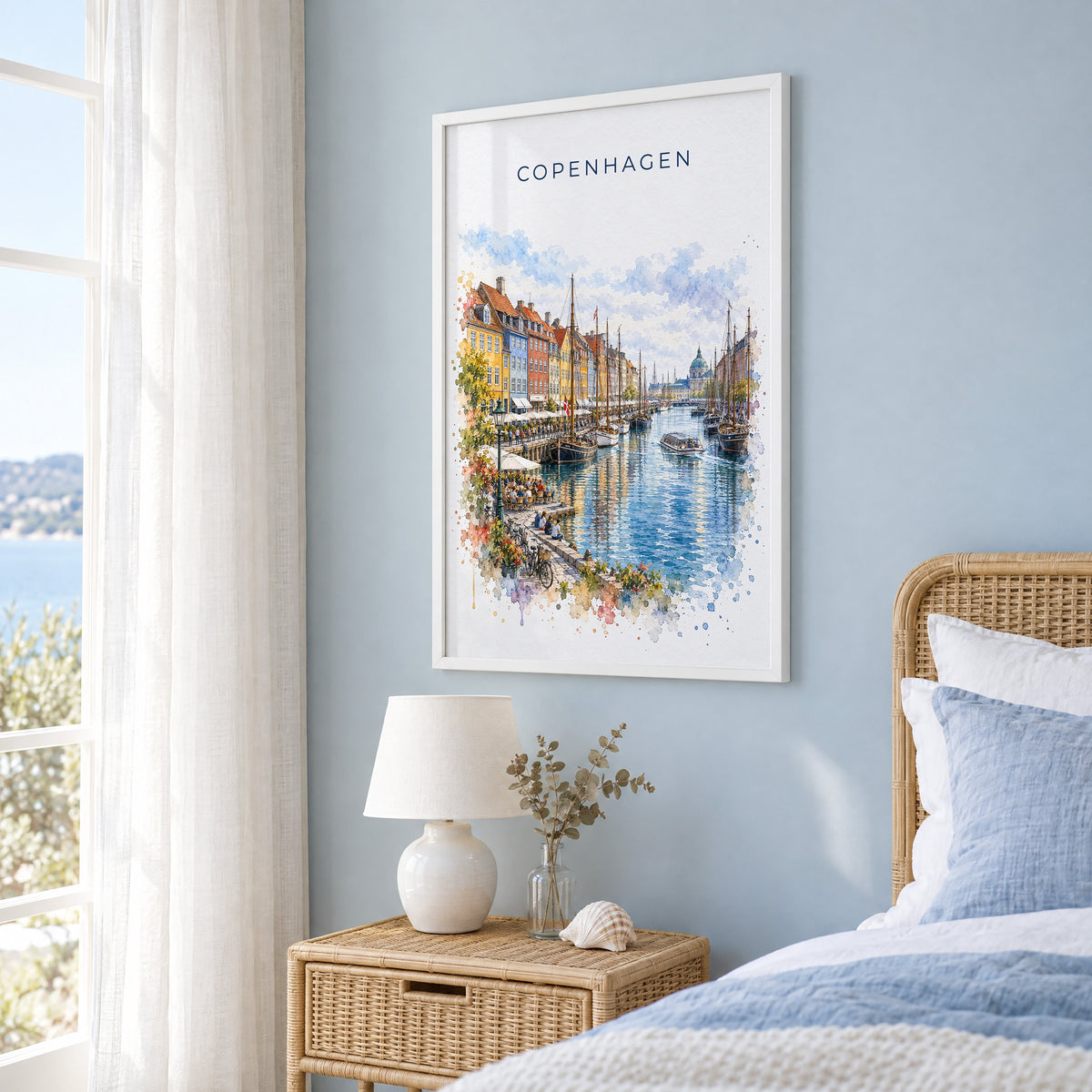 Copenhagen watercolor print in a white frame on a pale blue wall beside a rattan bed in a coastal bedroom
