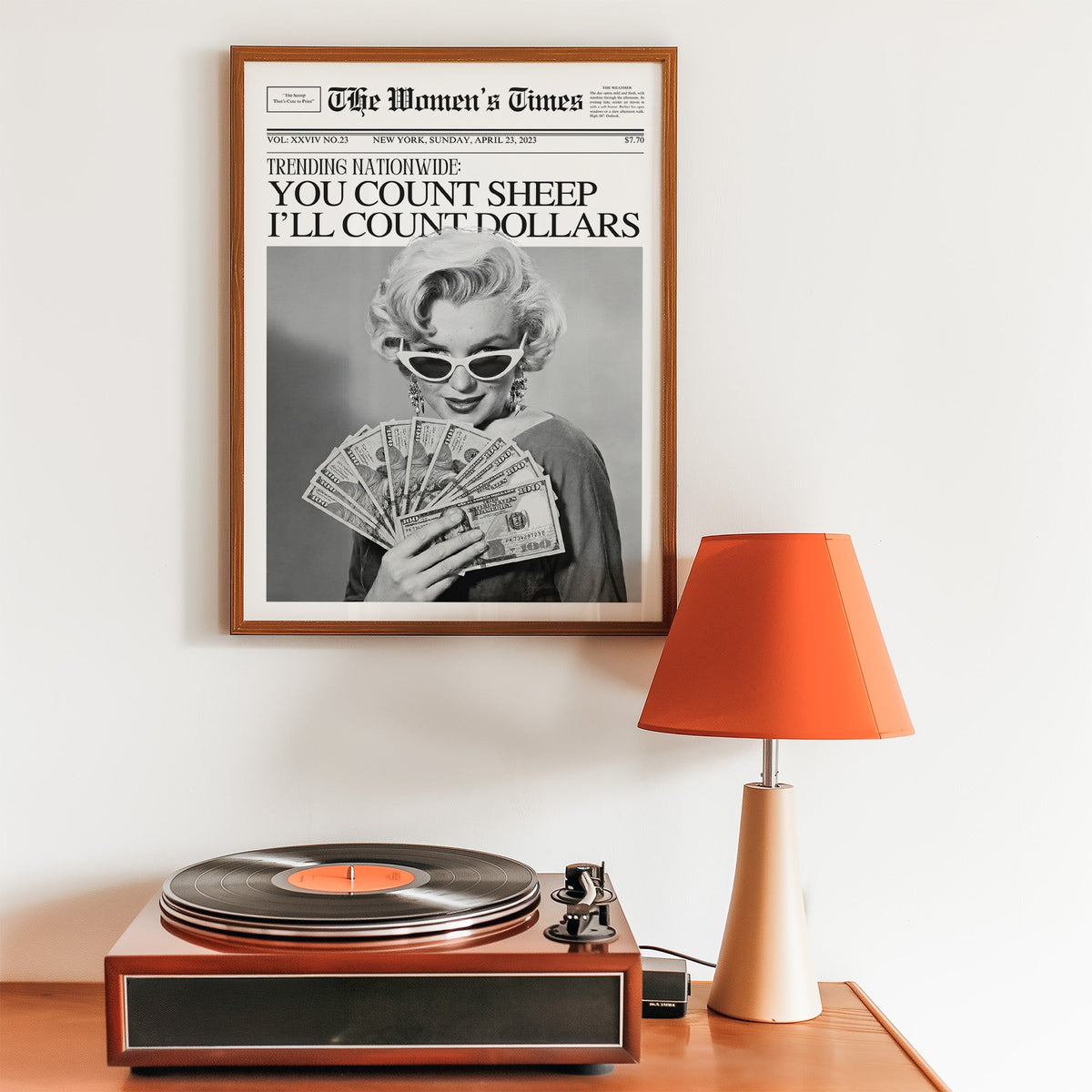 Woman fanning dollar bills mock front page print in a walnut frame above a record player and orange lamp