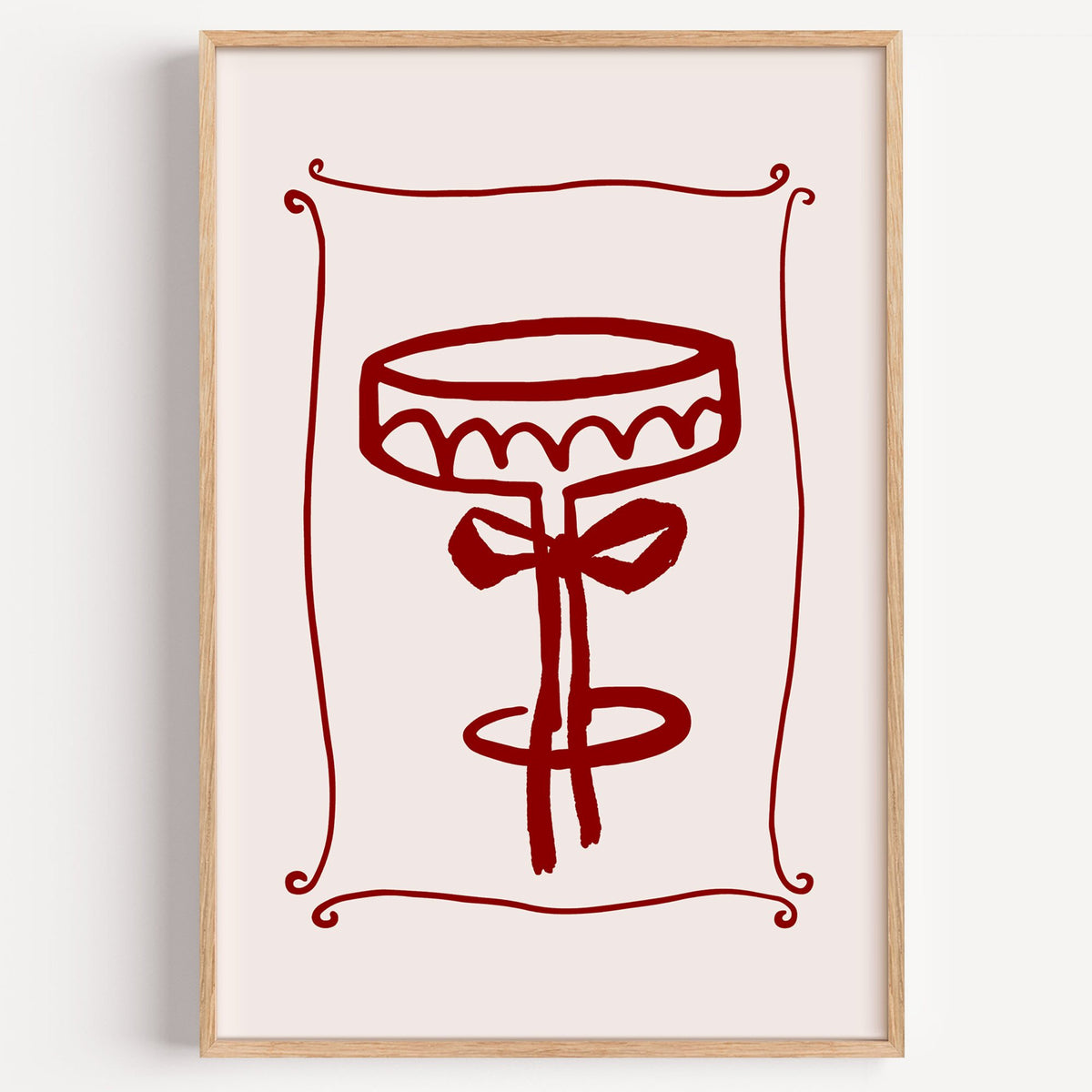 burgundy brush coupe glass with bow print in a light oak frame on a plain white wall