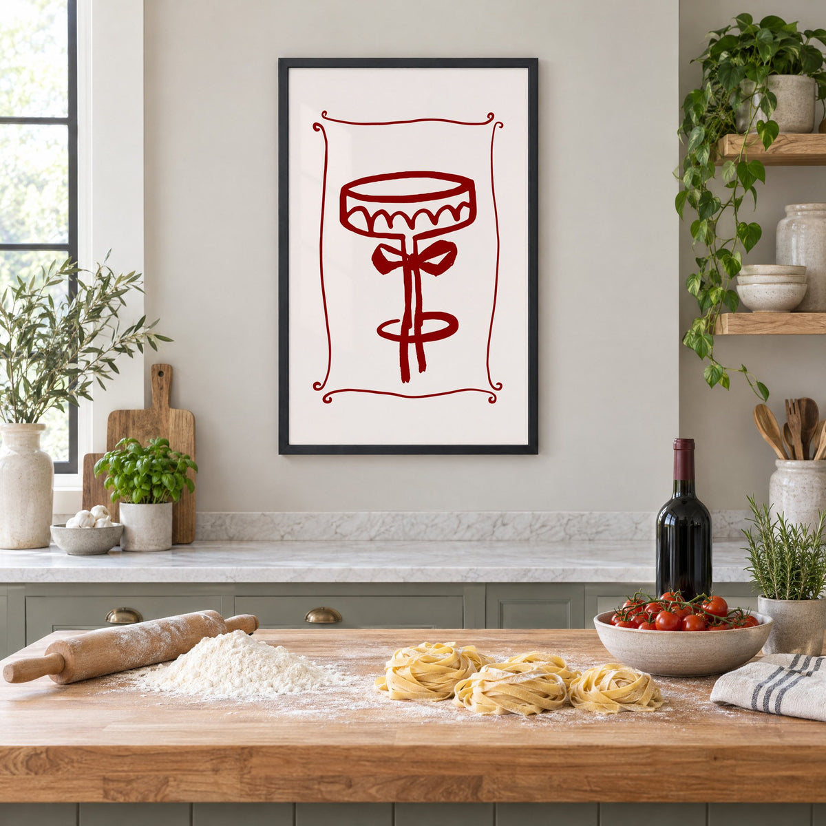burgundy brush coupe glass with bow print in a black frame above a butcher-block island with fresh pasta, flour and cherry tomatoes