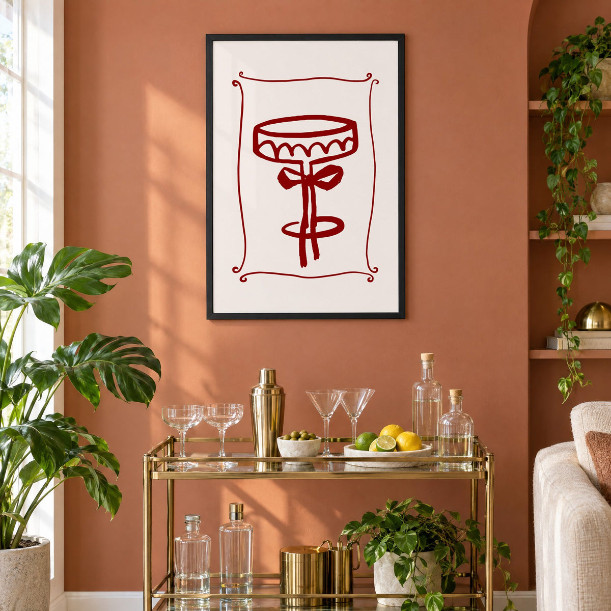 burgundy brush coupe glass with bow print in a black frame on a terracotta wall above a brass bar cart with coupes and citrus