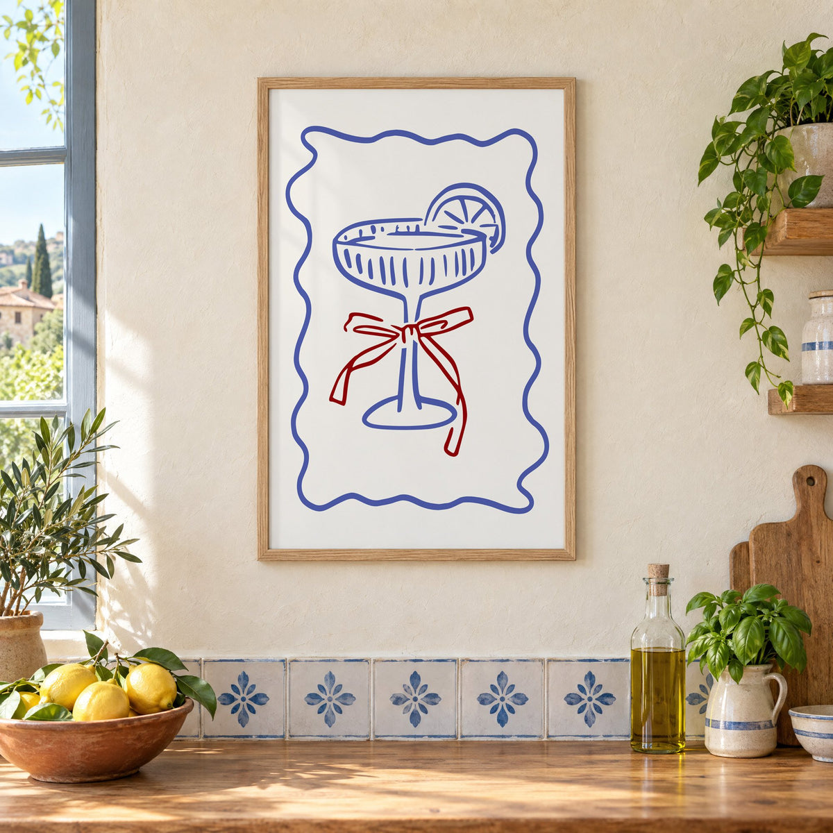 Blue coupe glass with red bow print in an oak frame on a cream plaster wall above a worktop with a bowl of lemons and blue-and-white tiles