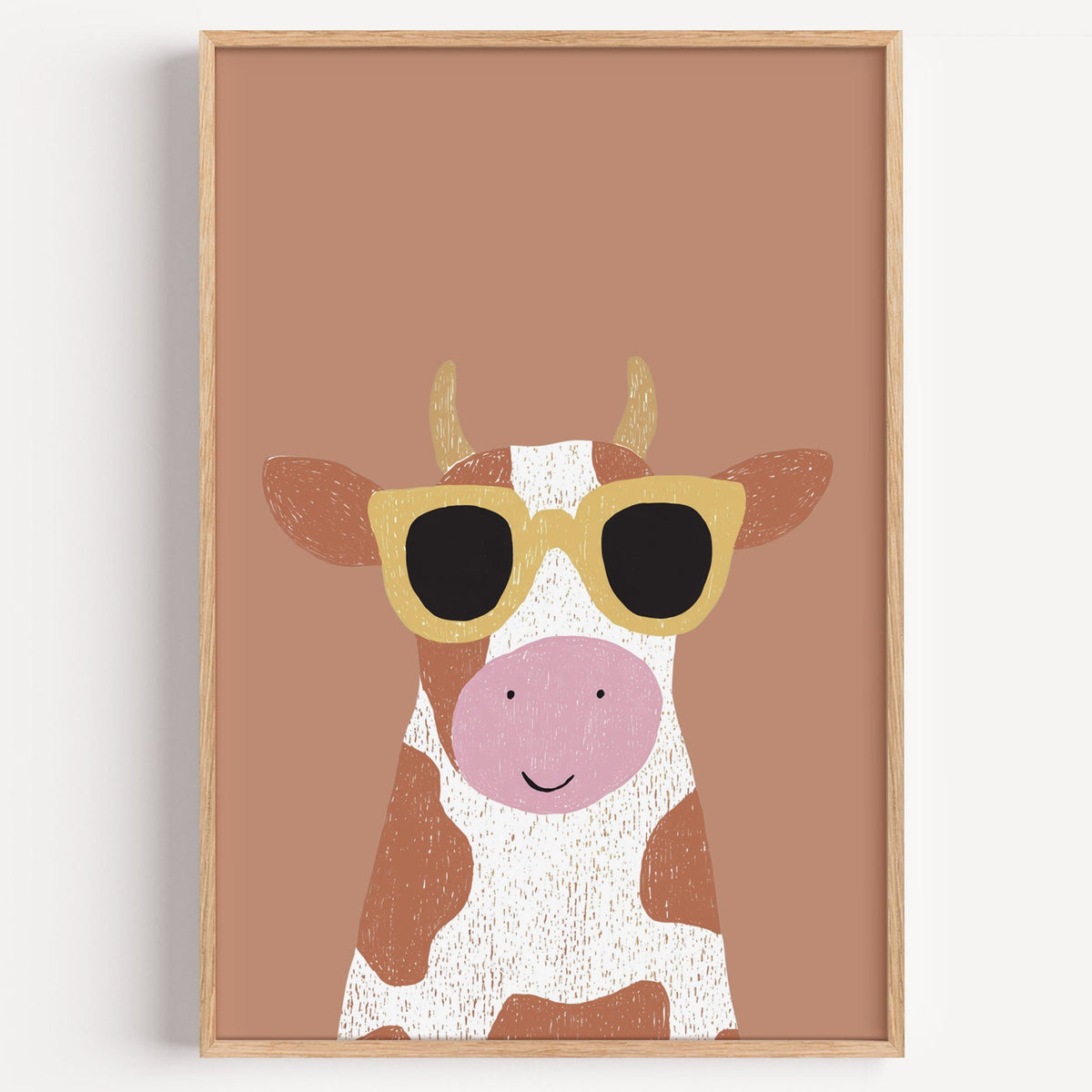Cow in yellow sunglasses nursery print in a light oak frame on a plain white wall
