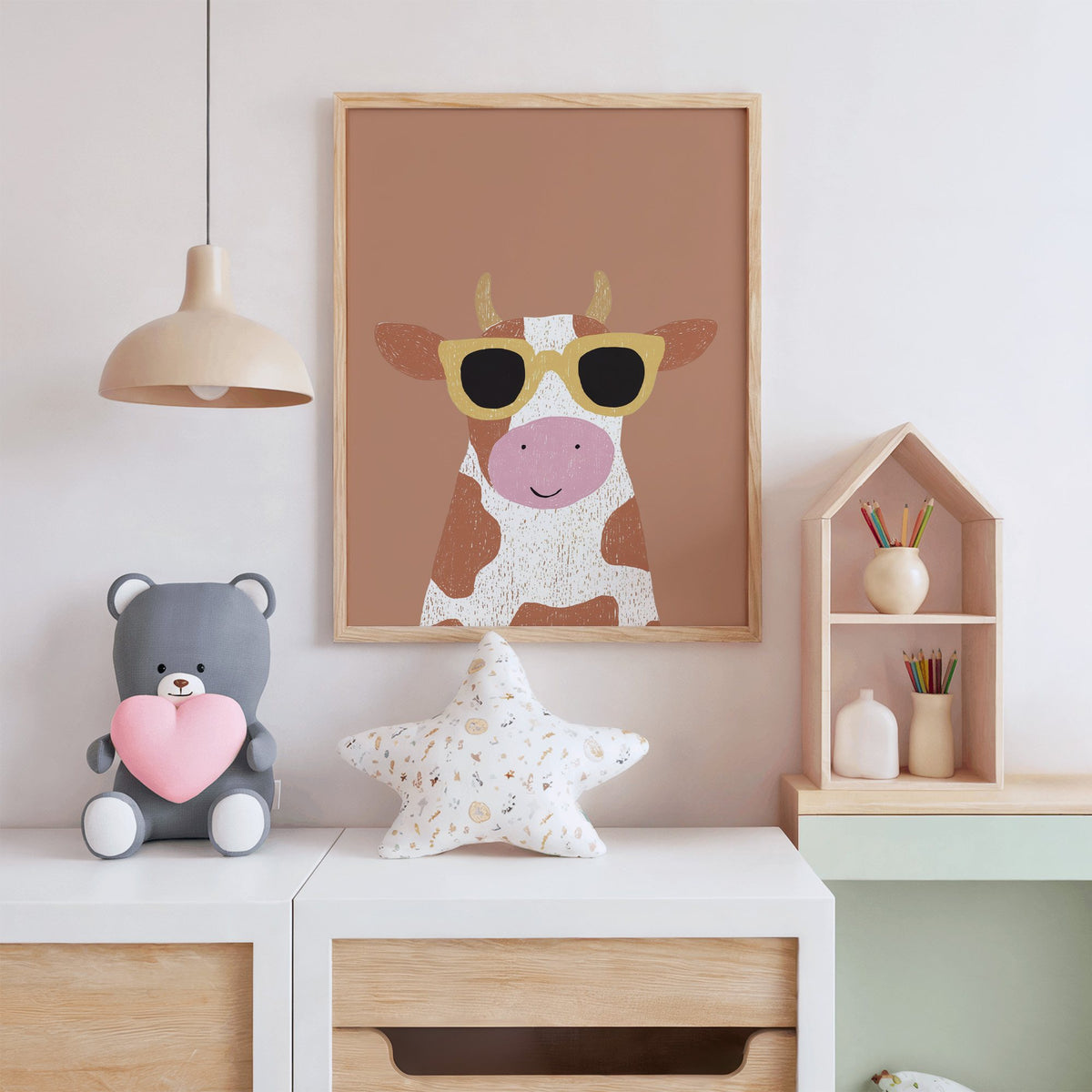 Cow in yellow sunglasses nursery print in an oak frame above a white dresser with a star pillow and house shelf