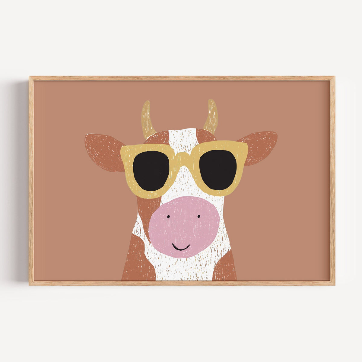Landscape cow in yellow sunglasses nursery print in a light oak frame on a plain white wall