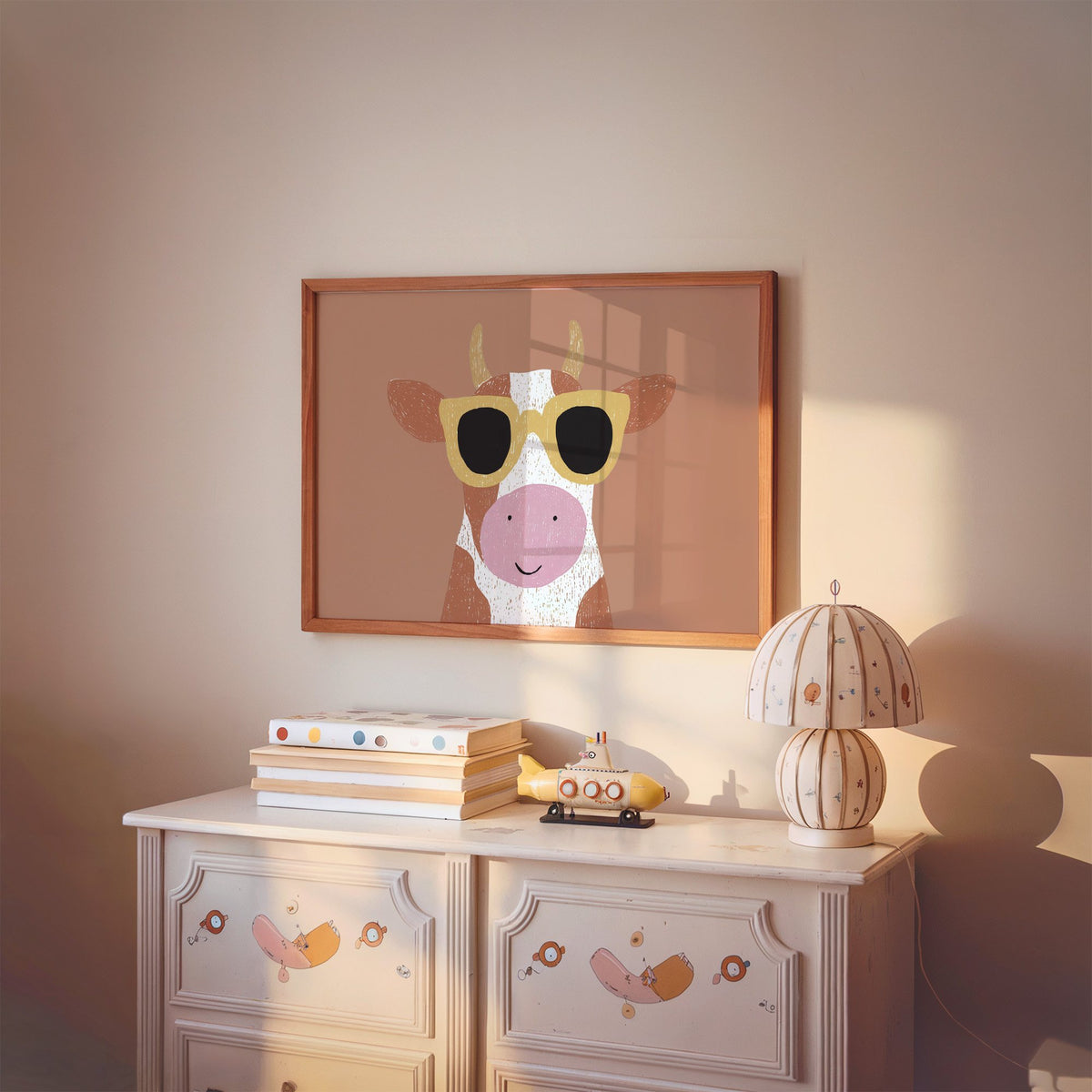 Landscape cow in yellow sunglasses nursery print in a cherry wood frame above a painted dresser and lamp
