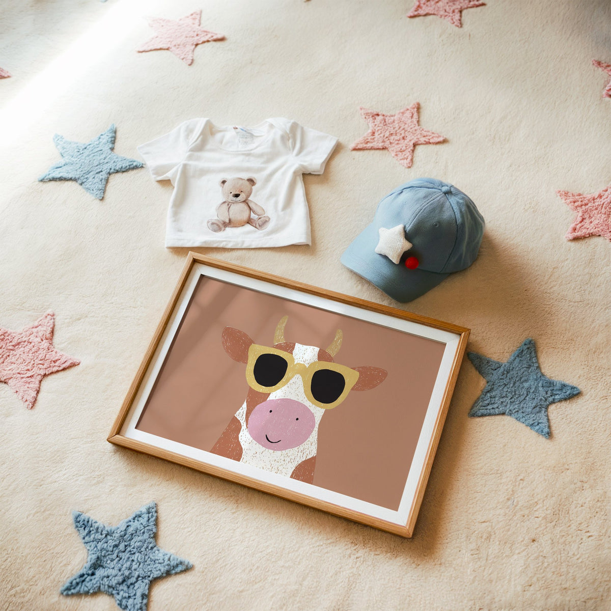 Landscape cow in yellow sunglasses nursery print in a matted oak frame on a star rug with a baby tee