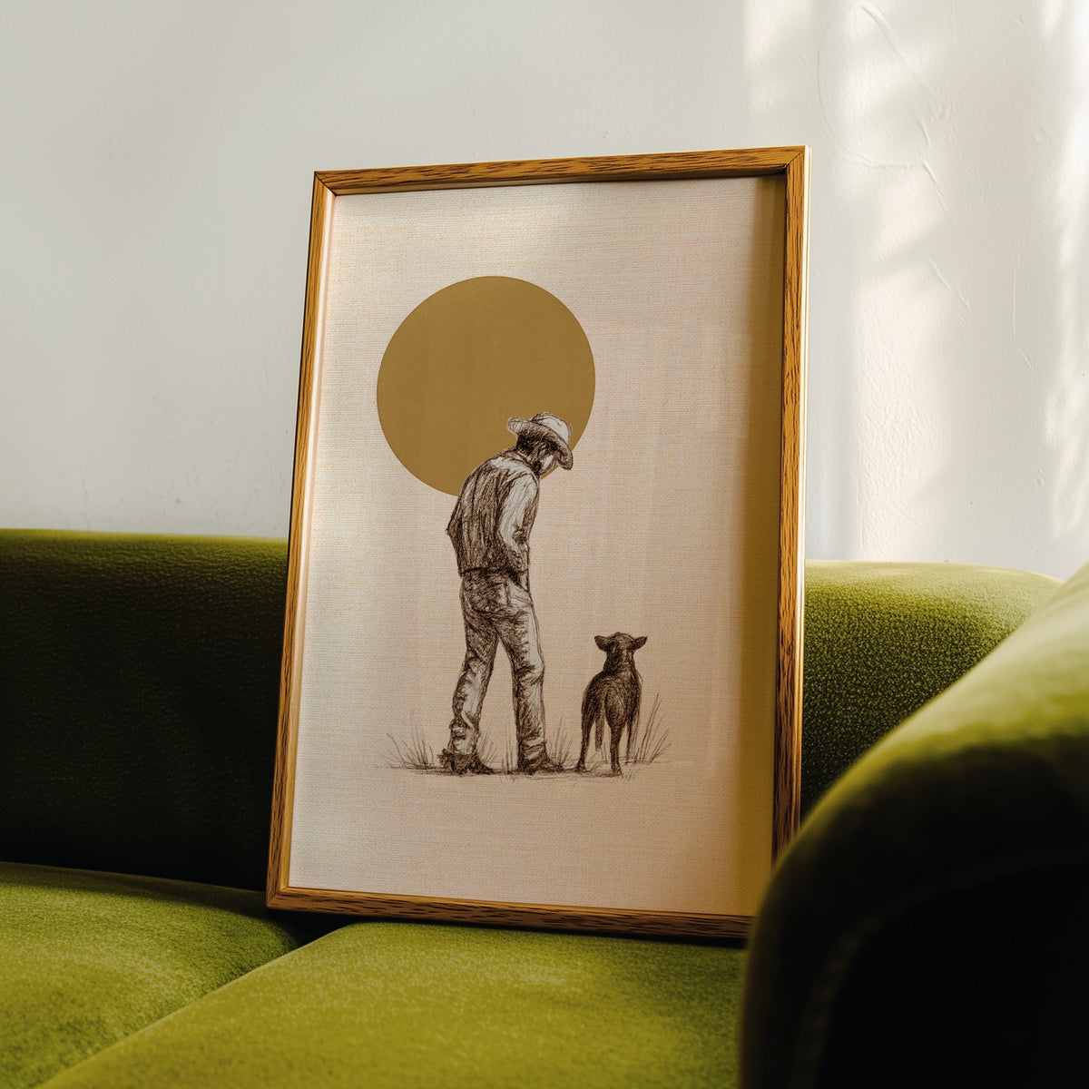 Cowboy and dog print in an oak frame leaning on a green velvet sofa