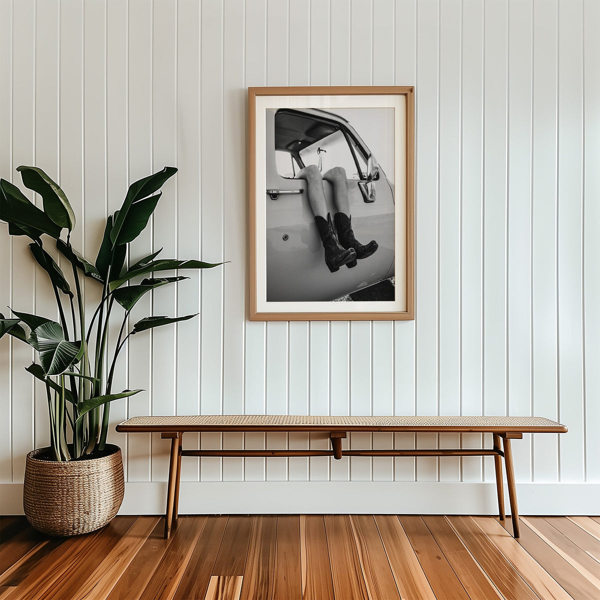 Cowboy boots dangling from a truck window print in a wood frame with a white mat above a cane bench