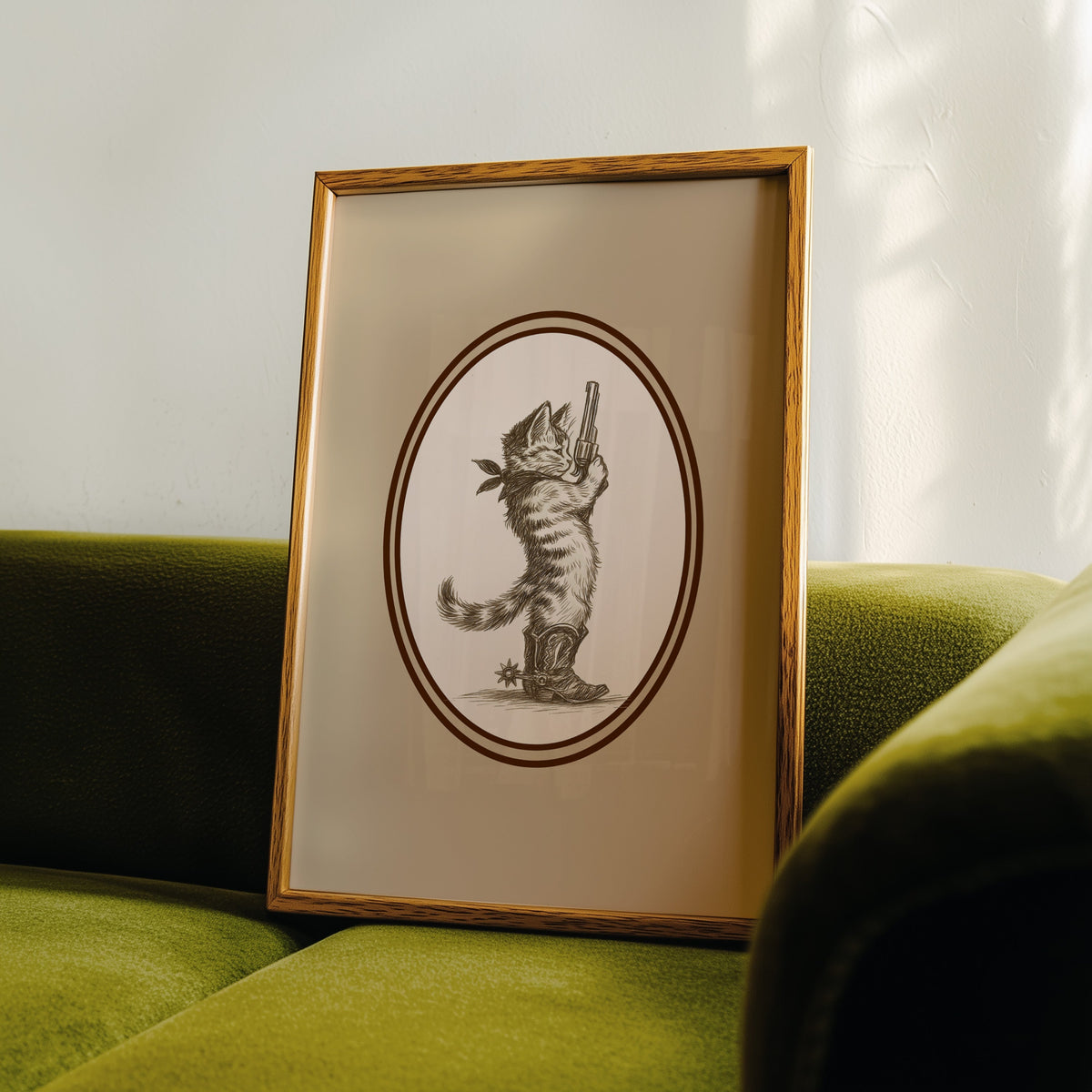Cowboy cat print in an oak frame leaning on a green velvet sofa