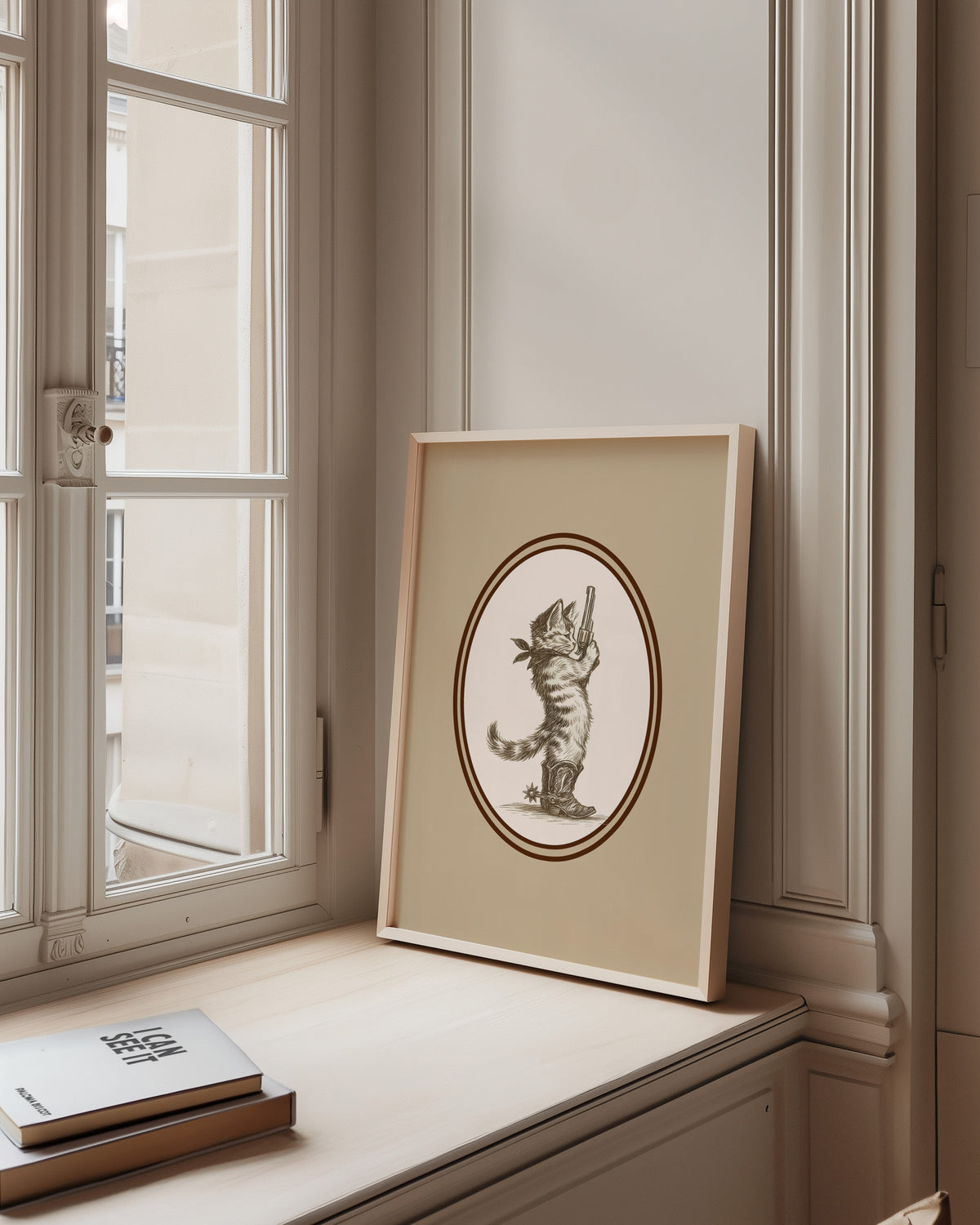 Cowboy cat print in a pale wood frame on a sunlit window ledge