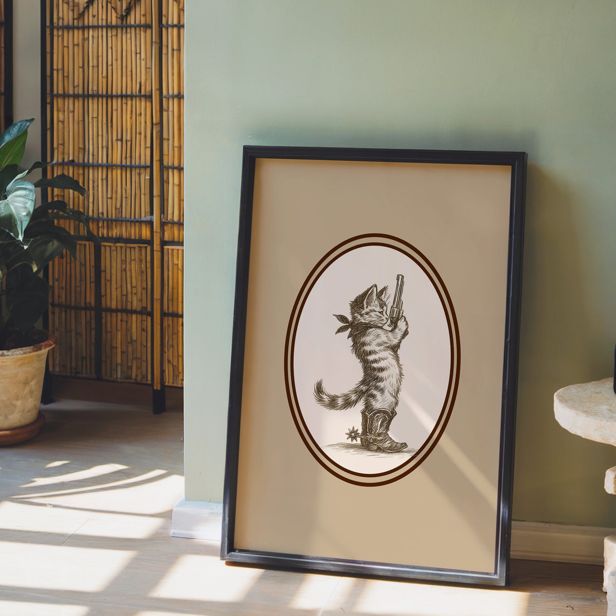 Cowboy cat print in a black frame leaning against a sage green wall