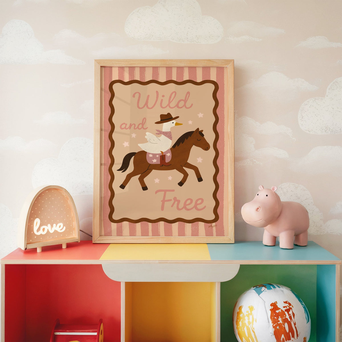 Cowboy goose riding a brown horse nursery print in an oak frame on a rainbow toy shelf against cloud wallpaper