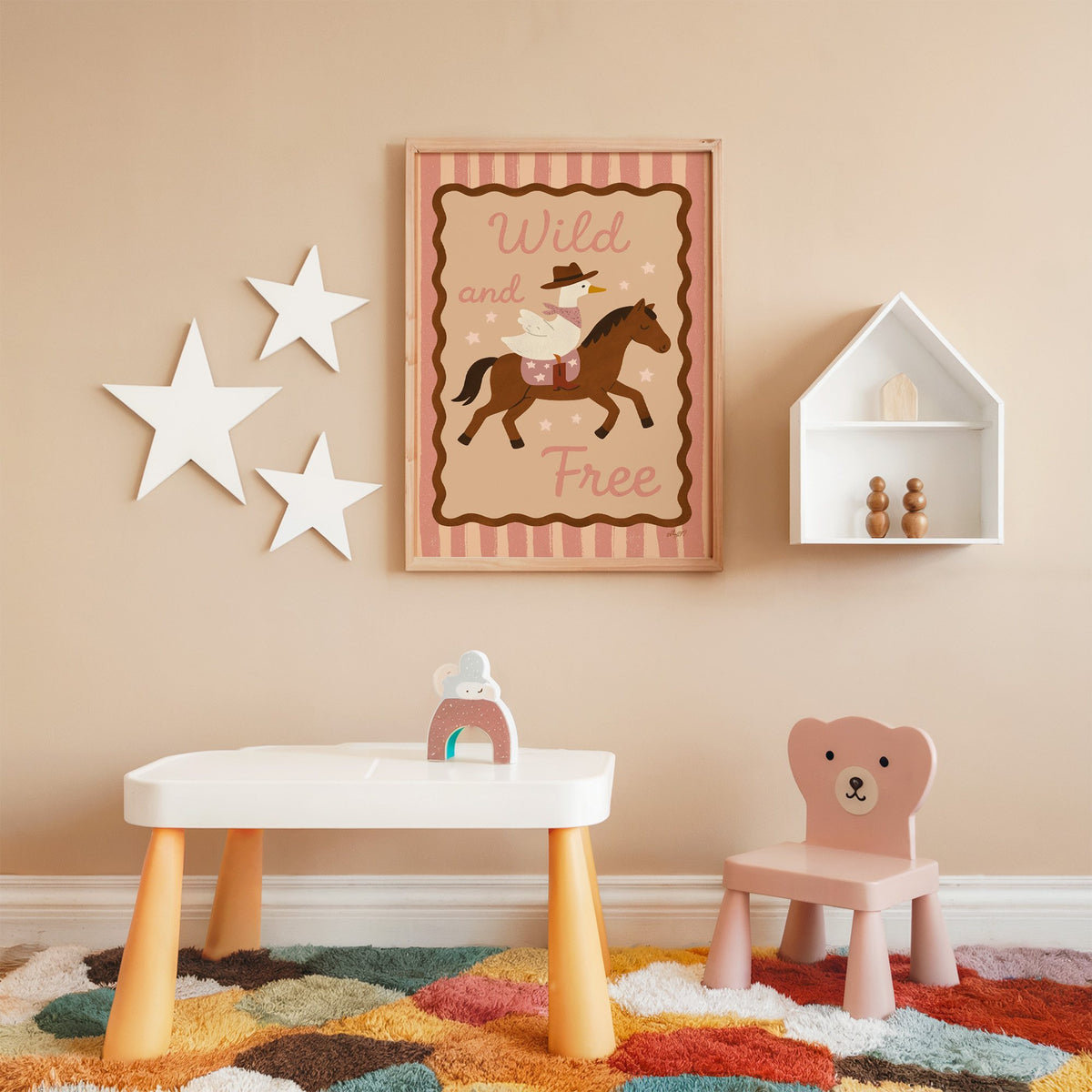 Cowboy goose riding a brown horse nursery print in an oak frame on a peach wall above a kids table with wall stars