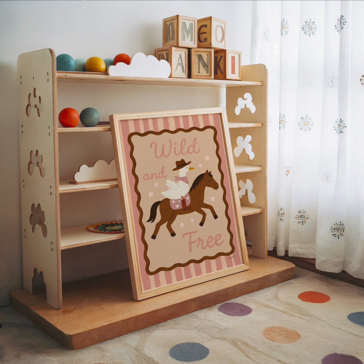 Cowboy goose riding a brown horse nursery print in an oak frame leaning on a toy shelf with wooden letter blocks