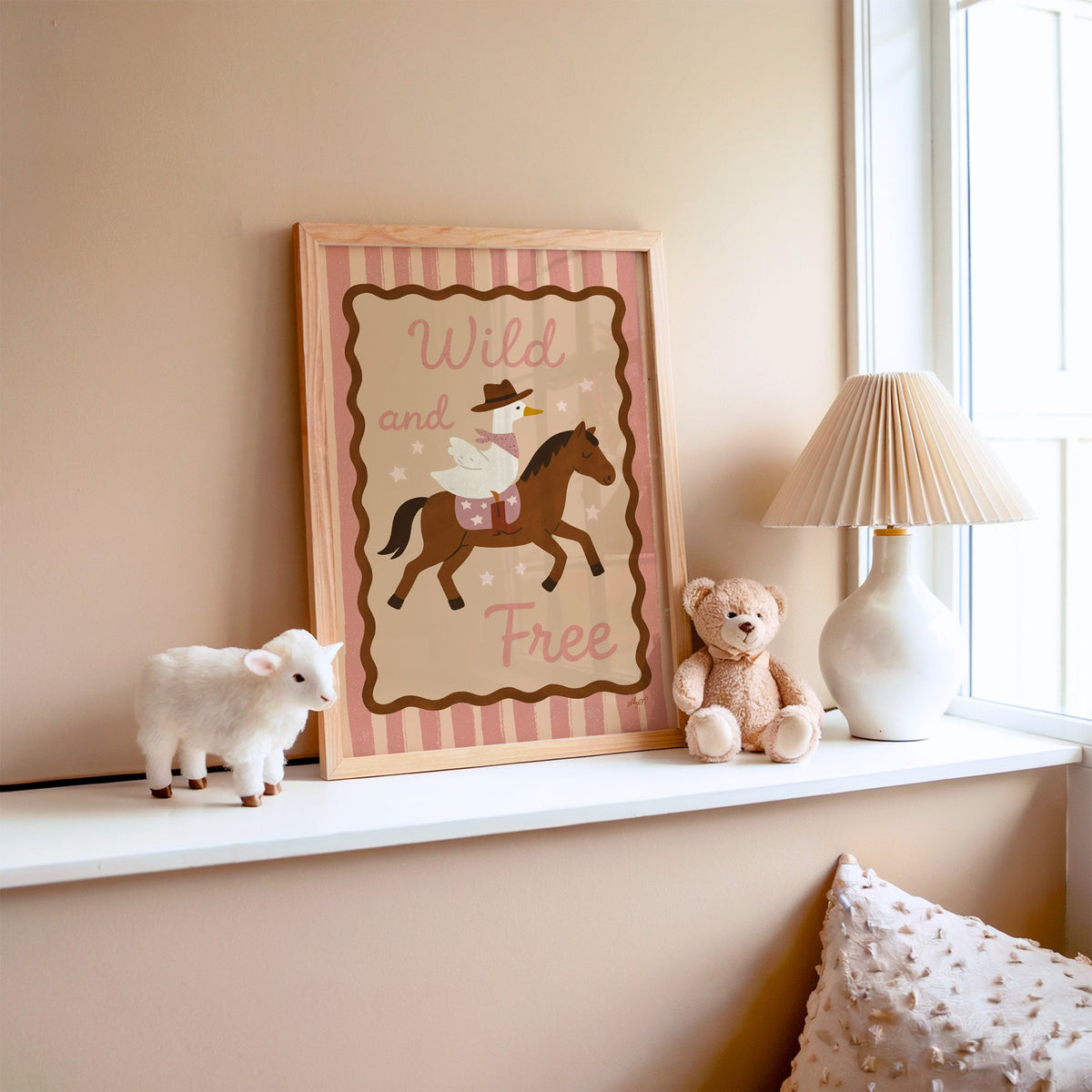 Cowboy goose riding a brown horse nursery print in an oak frame on a window ledge with a toy lamb and teddy