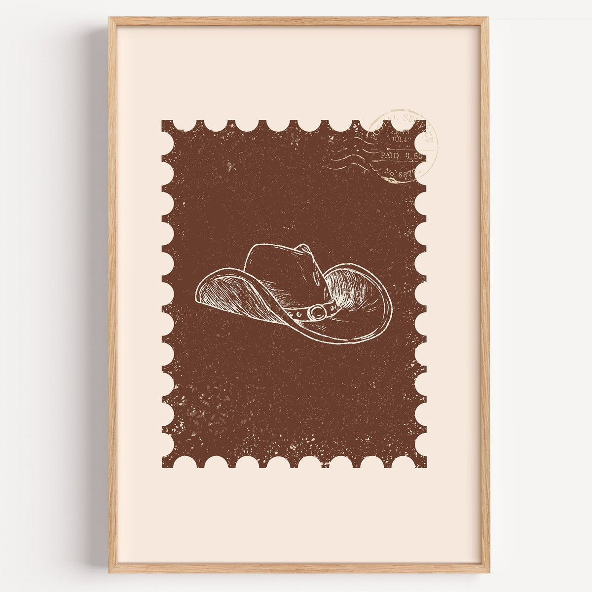Cowboy hat postage stamp print in a light oak frame on a plain white wall