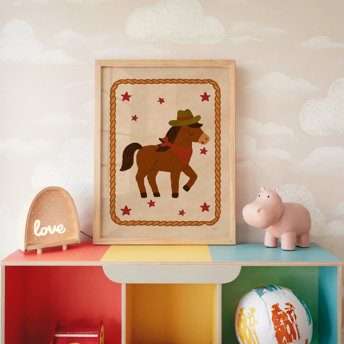 Cowboy pony in rope frame nursery print in an oak frame on a rainbow toy shelf against cloud wallpaper