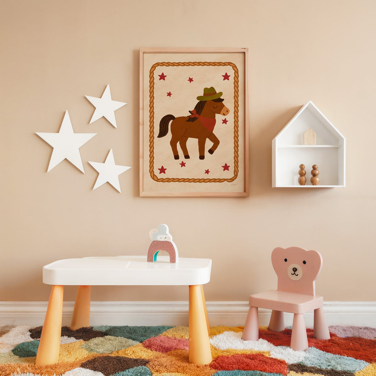 Cowboy pony in rope frame nursery print in an oak frame on a peach wall above a kids table with wall stars